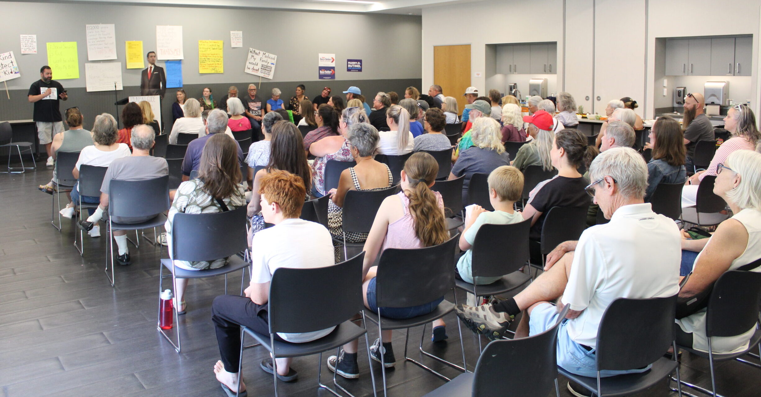 A group of Town Hall attendees listens to a speaker in front of protest signs